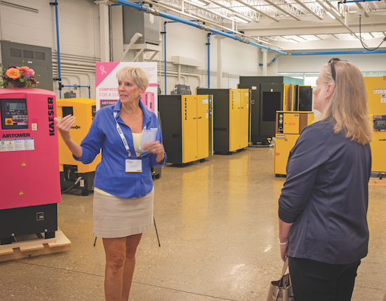 A woman presenting to a visitor in a showroom of compressor packages.
