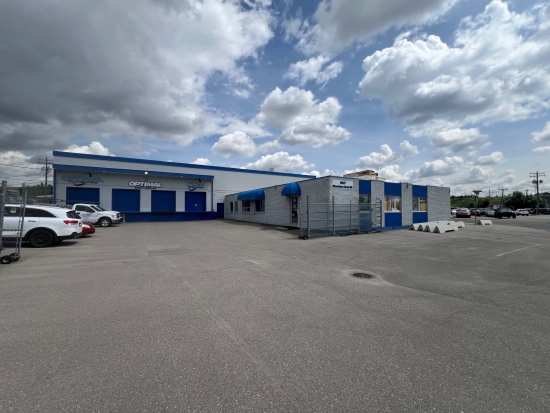 A single-storey blue and white industrial service building with a car park in front.