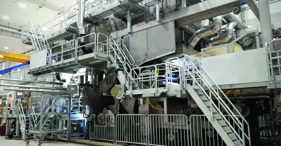 A paper machine with access stairs and walkways running the length of the mill hall.