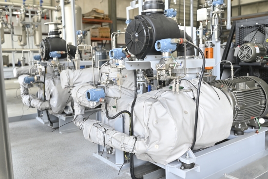 A row of insulated compressor packages on blue skids in a plant room, each with intake filter, instrumentation and drive motor.
