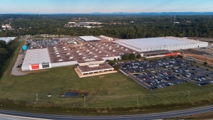 Aerial view of a manufacturing plant with a large roof, staff car park and loading yard.