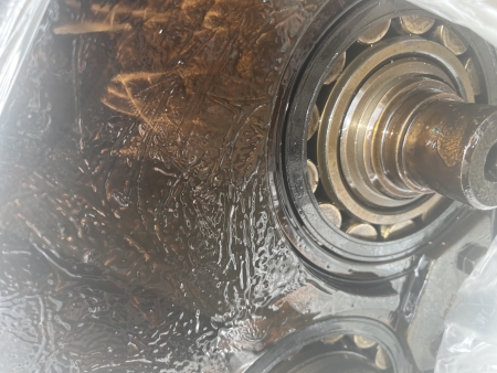A compressor bearing and gear assembly submerged in dark oil heavily contaminated with metallic debris.