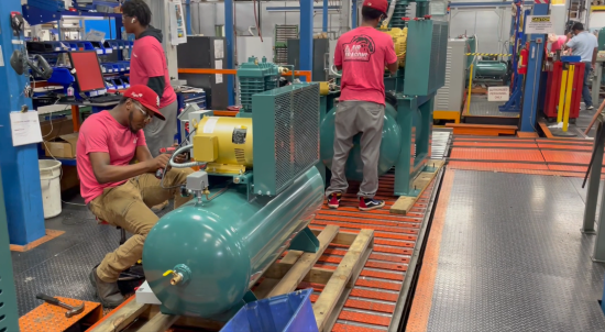 Workers assembling green tank-mounted compressor packages on a production line.