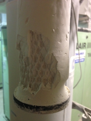 A compressed air pipe with its outer coating flaking away to expose a diamond-patterned inner surface.