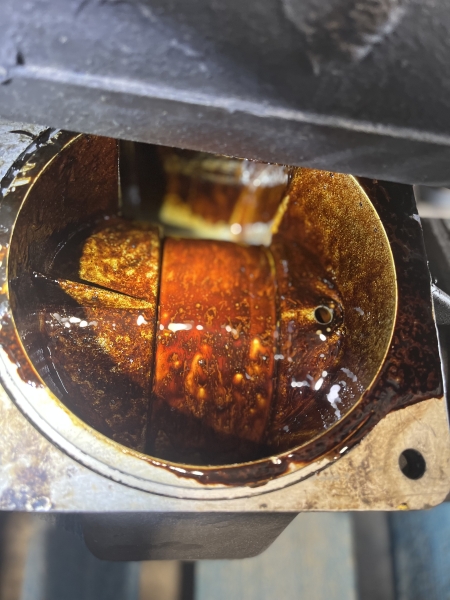 Looking down into a compressor sump, the internals coated in thick orange-brown varnish.