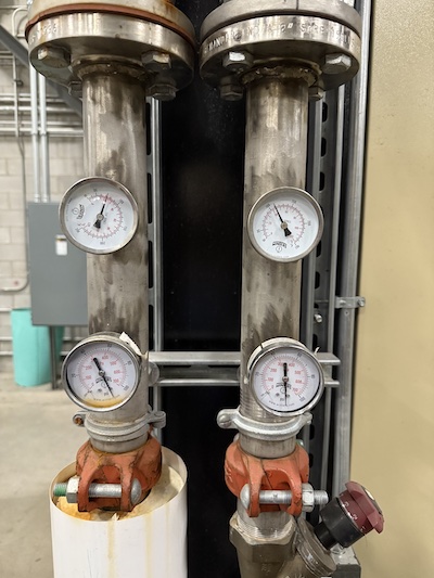 Two stainless steel filter housings with pressure gauges above and below, connected to orange grooved couplings.