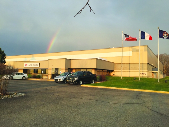 A single-storey industrial building with a rainbow behind it and three flags on poles at the entrance.