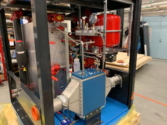 A skid-mounted heat exchanger package under construction, with plate exchangers, a red expansion vessel and instrumentation on a frame.