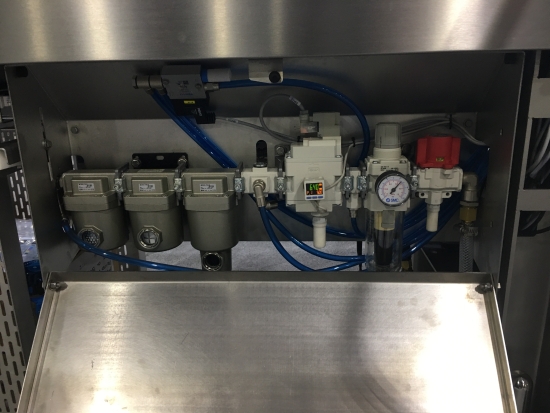 The pneumatic panel inside a packaging machine, with filter units, a valve manifold, regulator and pressure gauge plumbed in blue tubing.