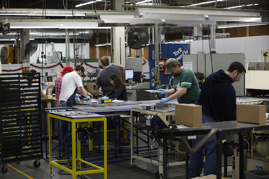 Workers assembling parts along a bench in a manufacturing area.