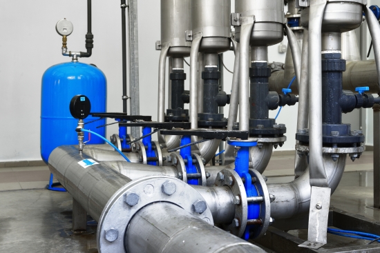 Industrial water treatment pipework with a blue pressure vessel, gauges and flanged headers in a boiler room.