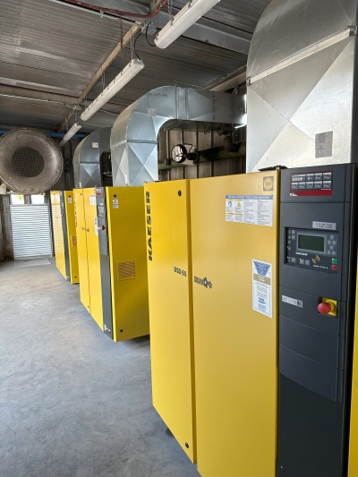 A row of Kaeser compressors in a plant room, each ducted to an overhead extract hood.