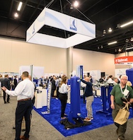 A trade show stand with blue equipment on display and visitors talking to staff.