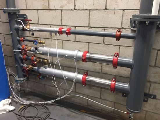 Three parallel pipe runs on a block wall, each with grooved couplings, isolation valves and instrument tappings wired back to a logger.