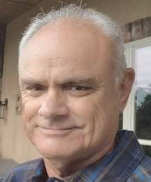 A man photographed outdoors in a checked shirt.