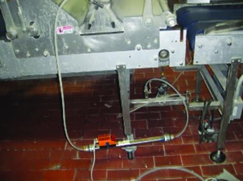 A flow meter fitted into a compressed air line beneath a production machine on a tiled floor.