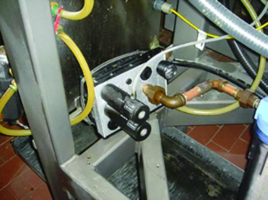A vacuum manifold and fittings mounted on a machine frame with braided hoses.